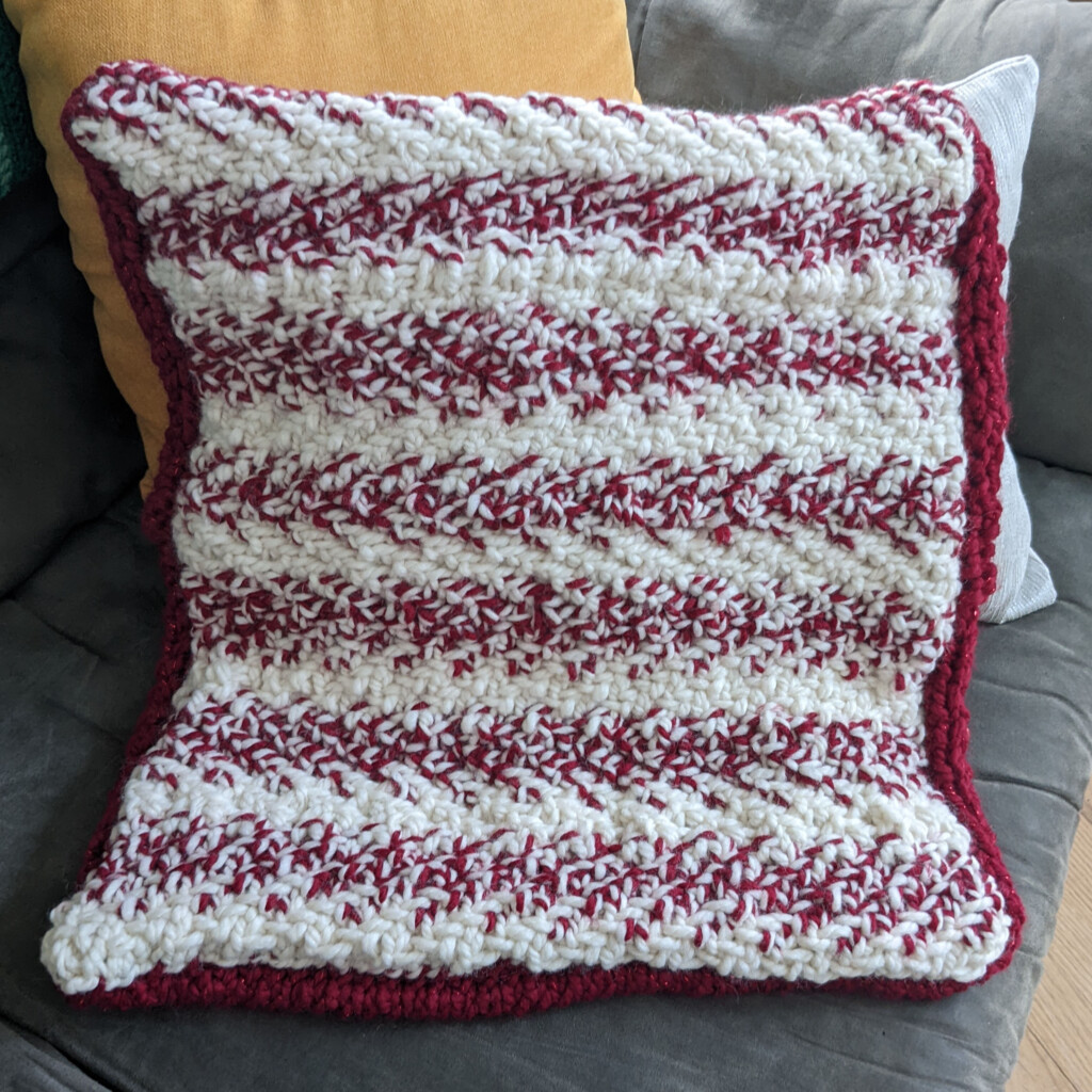 Image of a knit pillow case in a red and white striped yarn like a candy cane