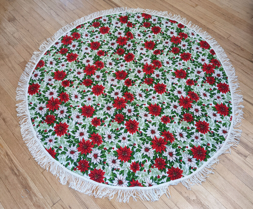 image of a round tablecloth with red and white poinsettias and white fringe on a wood floor