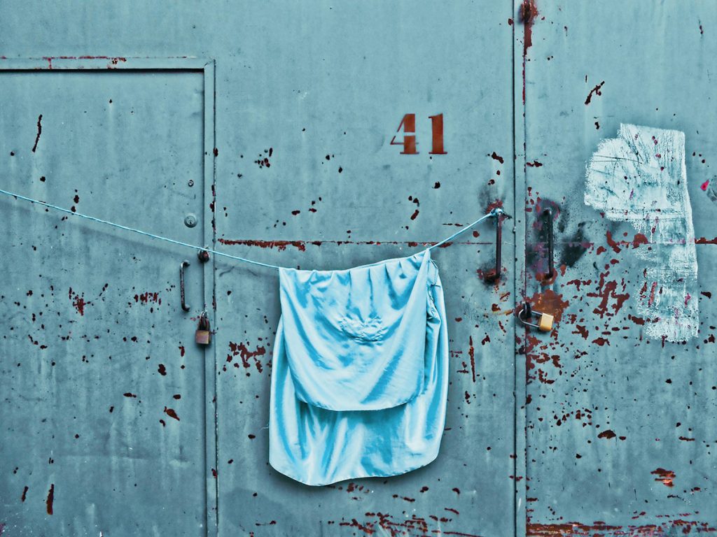 light blue towel hung out to dry on a rope in front of an industrial rusty blue wall