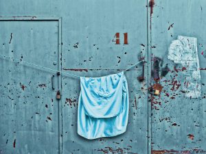 light blue towel hung out to dry on a rope in front of an industrial rusty blue wall
